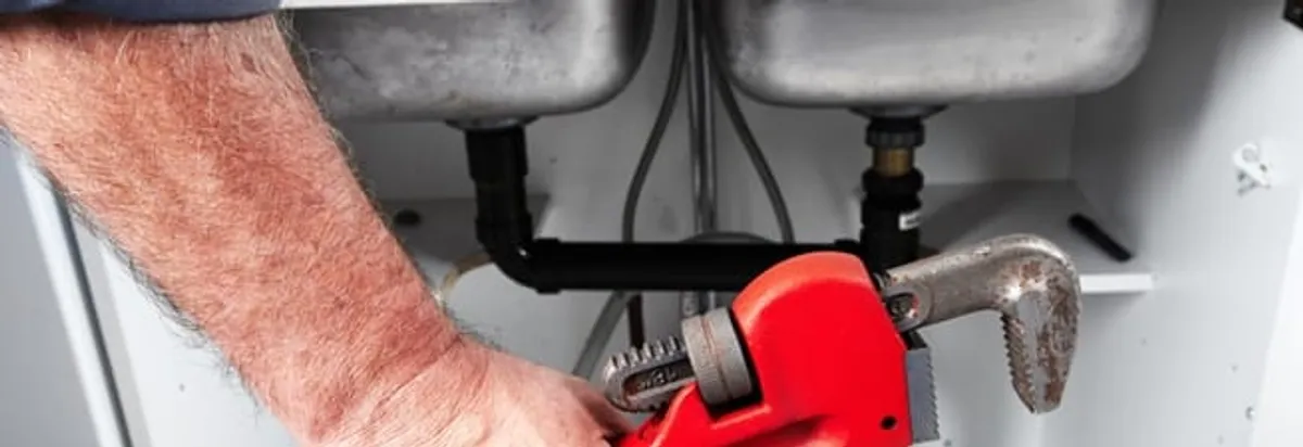 Garbage disposal repair technician tightening drain connections under a kitchen sink in Glendale, AZ