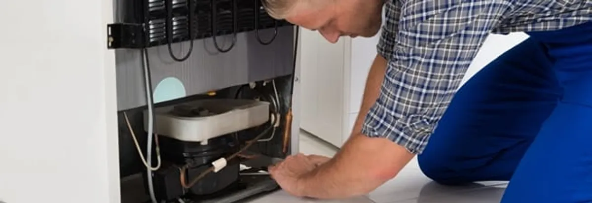 Refrigerator repair technician servicing the compressor and condenser area in Glendale, AZ